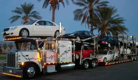 Professional luxury car carrier truck with premium vehicles under palm trees